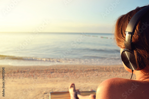 Young woman in headphones listening music and enjoying beautiful views sea, rear view.