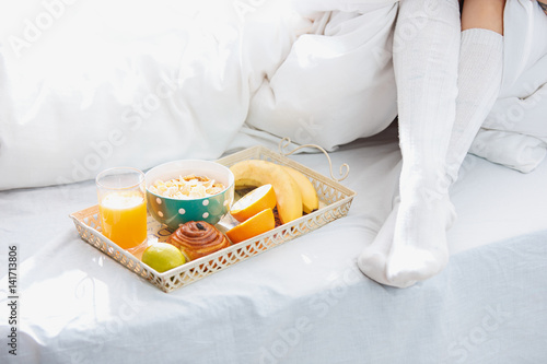 Partial view of female legs and breakfast on bed