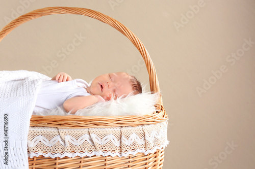 Cute little baby sleeping in wicker basket on color background