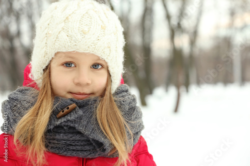 Portrait of cute little girl in beautiful warm outfit on winter background