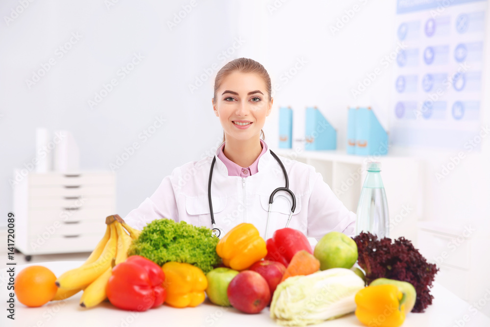 Young female nutritionist with vegetables and fruits in her office
