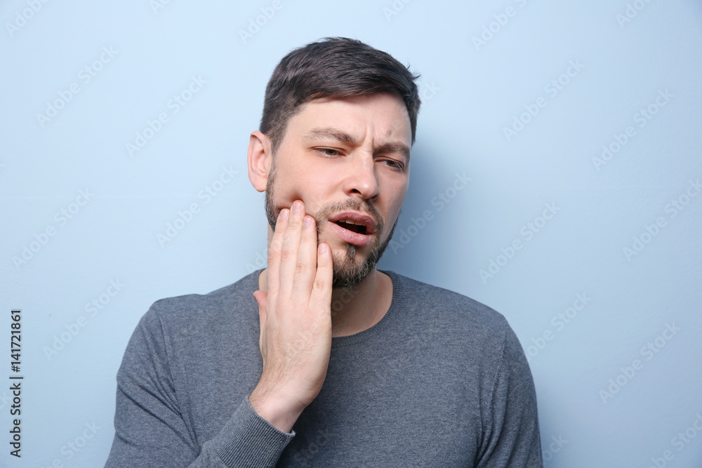 Handsome man suffering from toothache on color background