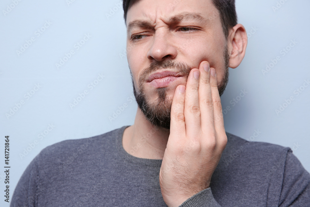 Handsome man suffering from toothache on color background