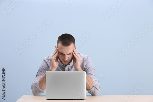 Quadro su tela Handsome young man suffering from headache while working with laptop, on color b