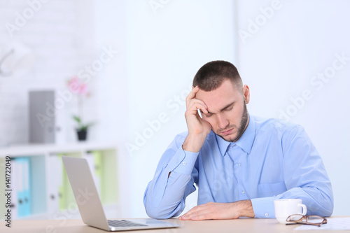 Handsome young man suffering from headache while working in office