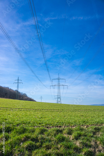 Bodennahe Aufnahme von Hochspannungsleitungen vor strahlend blauem Himmel