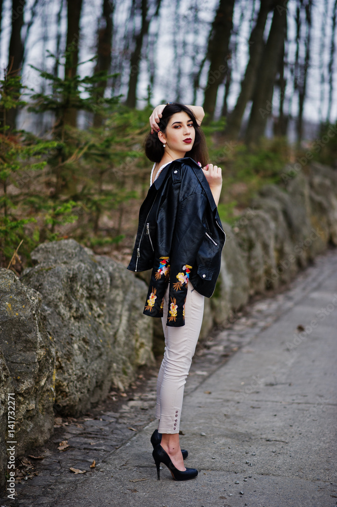 Brunette gypsy girl posed against stones on park. Model wear on leather jacket and t-shirt with ornament, pants and shoes with high heels. Brunette gypsy girl posed against stones on park. Model wear on leather jacket and t-shirt with ornament, pants and shoes with high heels.