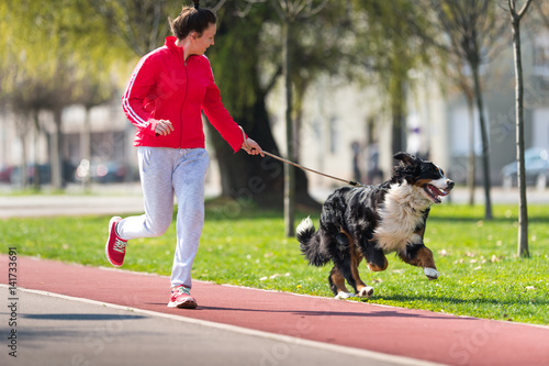 Young pretty girl running outdoor with her Bernese Mountain dog