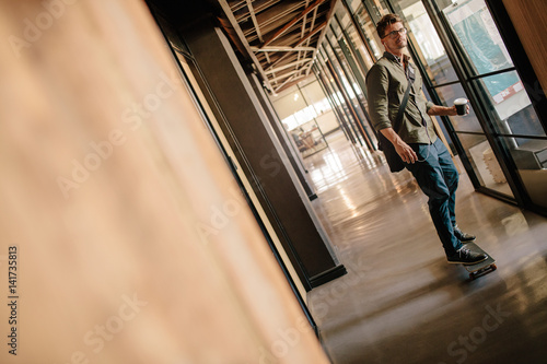 Handsome young man skateboarding in office corridor