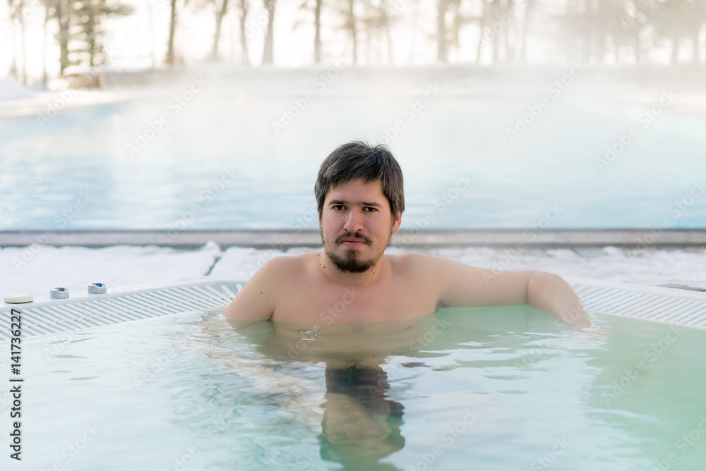 Young man in bathtub jacuzzi outdoors at winter day