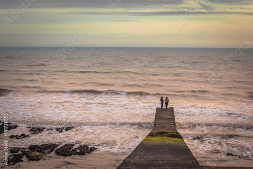 9th march  2017 Brighton  UK. Two girls looking towards the sea on a cement platform at Rottingdean beach.