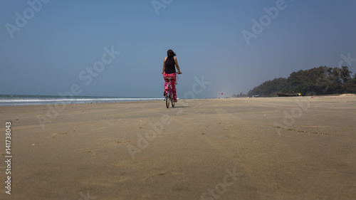 Girl riding a bicycle on a beach in Goa, India