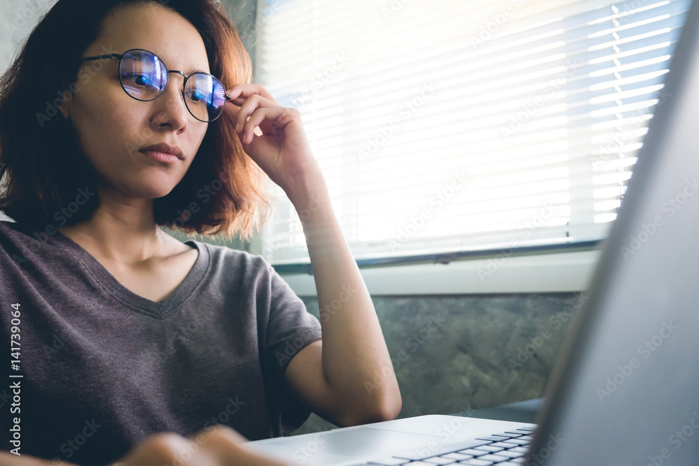 Casual young woman adjusting her glasses and using a laptop on the desk. Casual young woman adjusting her glasses and using a laptop on the desk.