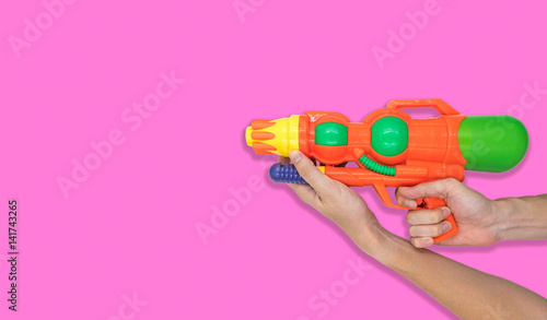 Hand holding gun water toy on pink background. Free space for text