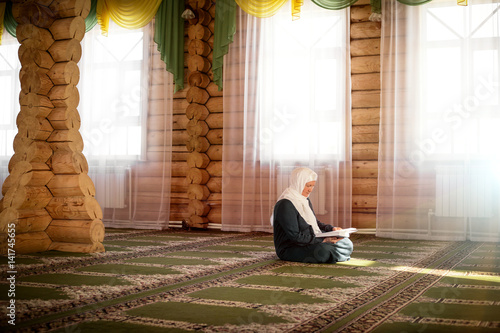 Elderly woman praying in the mosque and reading the Quran photo