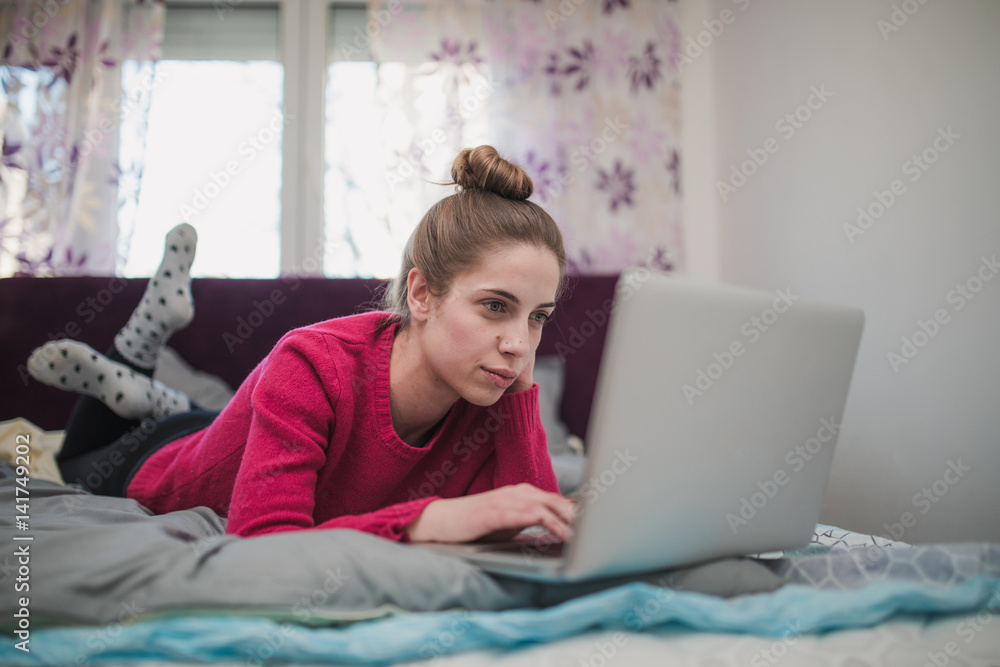 Beautiful woman working on laptop and lying on bed in bedroom Beautiful woman working on laptop and lying on bed in bedroom