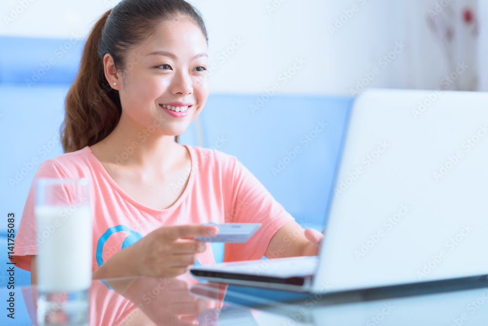 Asian Chinese young woman using laptop and credit card in home. Asian Chinese young woman using laptop and credit card in home.