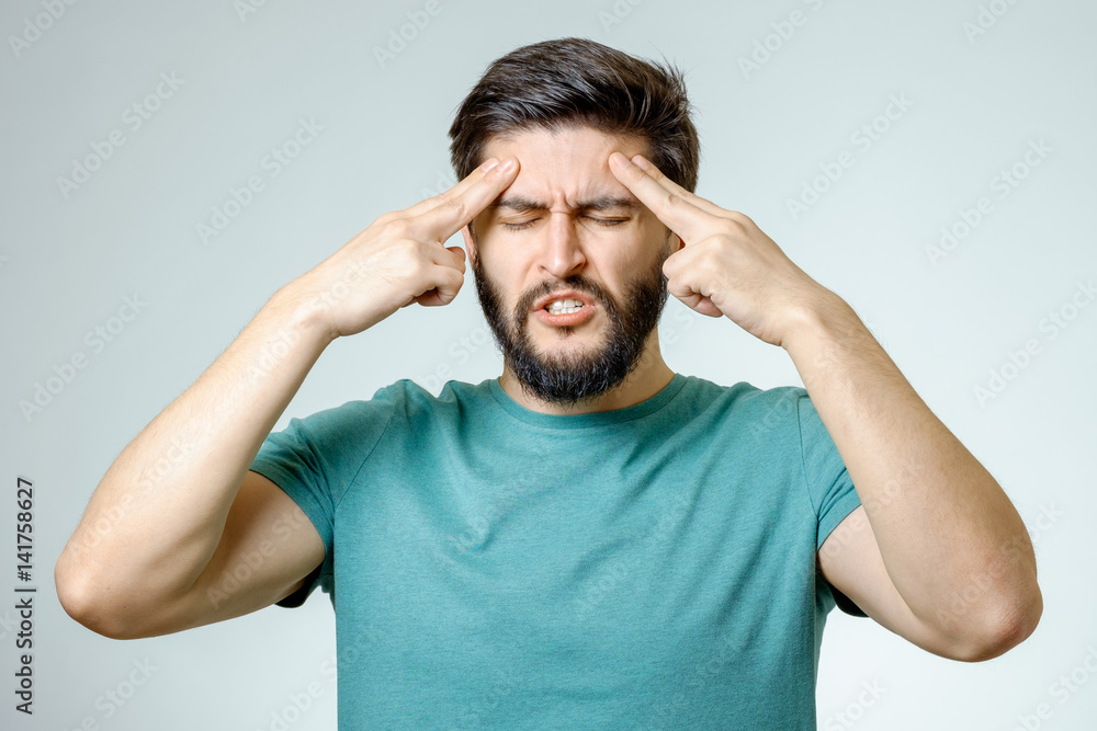 Young depressed handsome bearded man touching his head and having a headache over gray background Young depressed handsome bearded man touching his head and having a headache over gray background