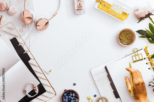 Desktop flatlay scene, with white open planner, desk tidy tray holding folded paper and black dividers, gold and rose gold stationery accessories featuring a female hand photo