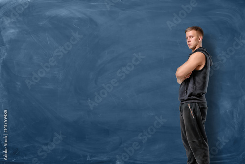 Muscular young man is standing his arms crossed and looking forward on blue chalkboard background © gearstd