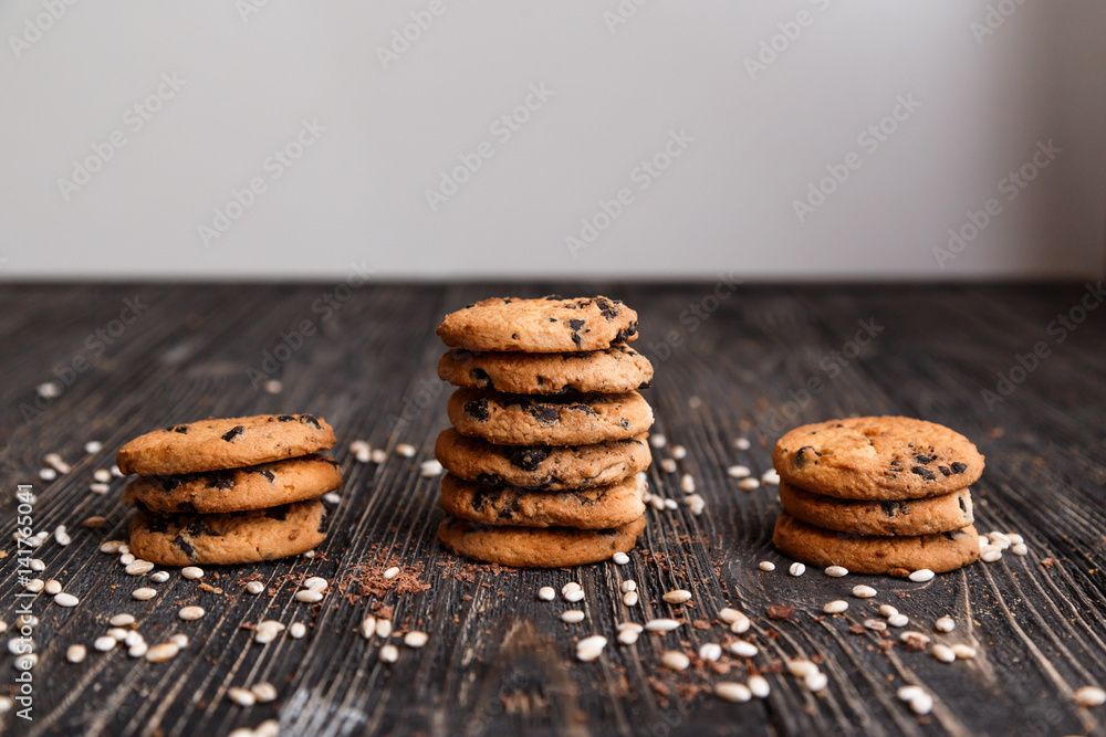 Three stacks of crisp chocolate chip cookies on a dark wooden table.