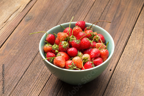 Fresh ripe strawberries in small green bowl on wooden.