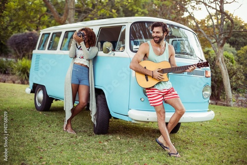 Tablou canvas Man playing guitar near campervan with woman