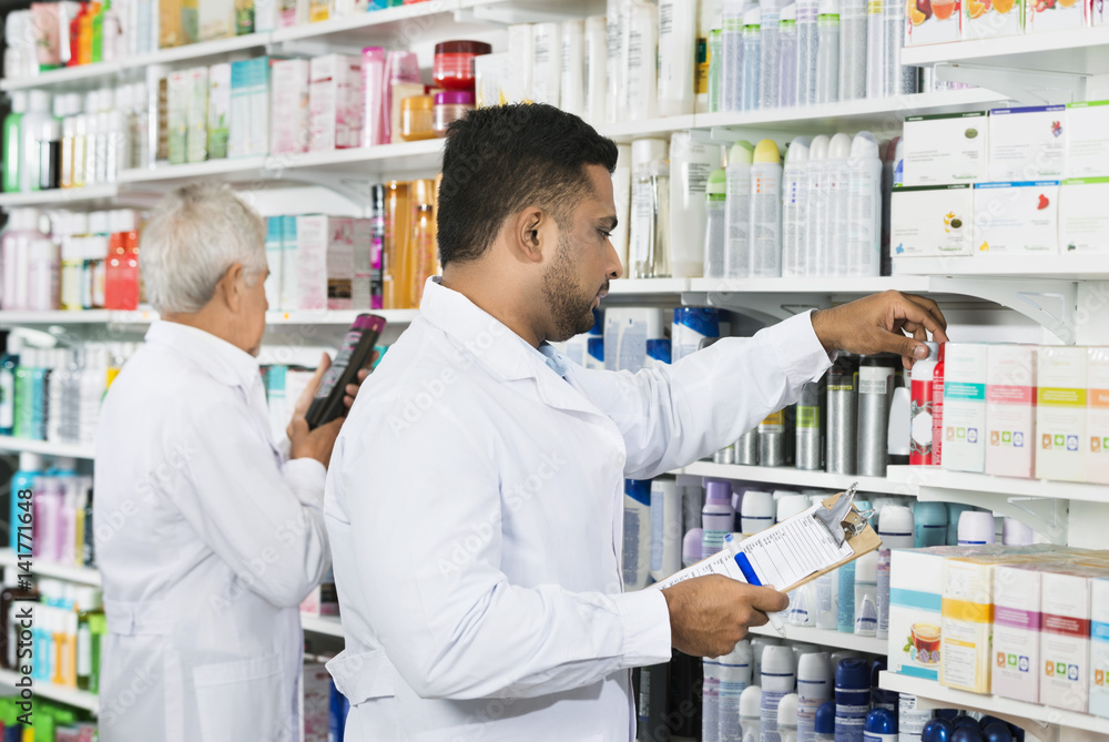 Chemist Counting Stock With Colleague In Pharmacy