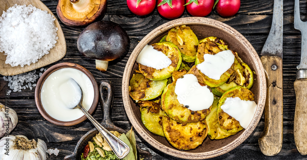 fried zucchini with sour cream and spices on wooden table, top view