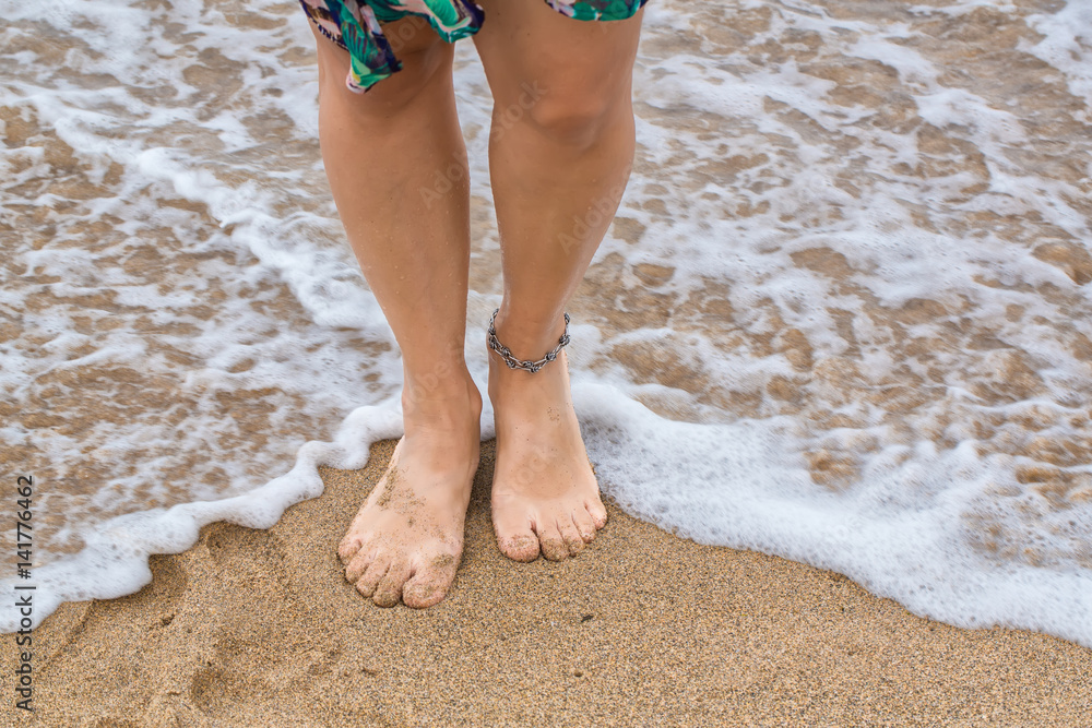 Female feet barefoot with anklet standing in waves on the surf line ...