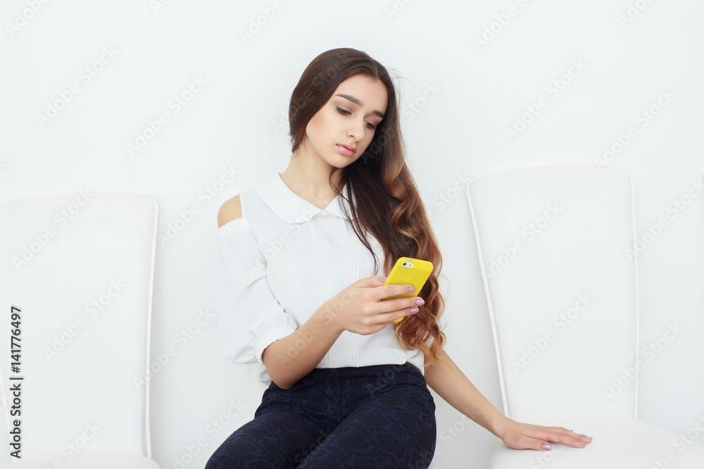 Smiling young businesswoman sitting on chair in modern office, using smartphone and writing in notepad Smiling young businesswoman sitting on chair in modern office, using smartphone and writing in notepad