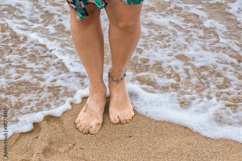 Fotografie Female feet barefoot with anklet standing in waves on the surf line