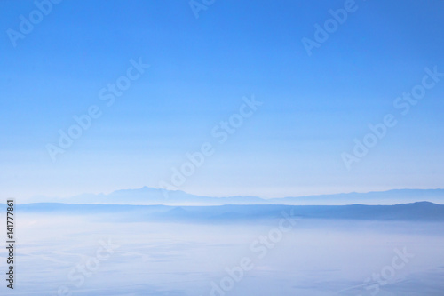 View on island hills and mountains in bright morning mist, fog or clouds above the sea as a minimalistic summer background