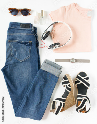 Stylish female clothes set. Woman/girl outfit on white background. Blue jeans, pink t-shirt, stripe wedges, headphones, hand watch and retro sunglasses. Flat lay, top view
