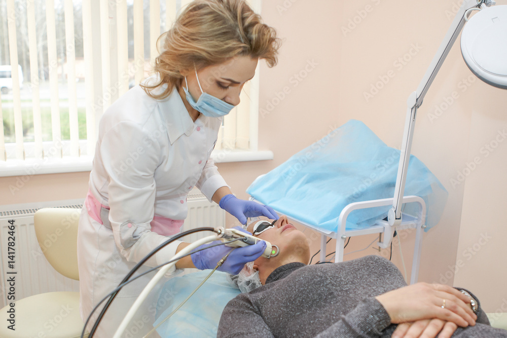 Obraz premium Therapist beautician makes a laser rejuvenation for the Woman by apparatus in a beauty salon.