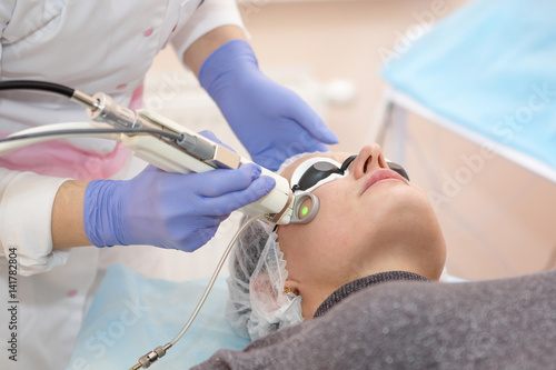 Therapist beautician makes a laser rejuvenation for the Woman by apparatus in a beauty salon.