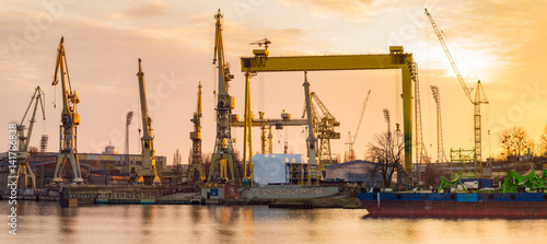 Fotografie, Obraz Silhouettes of cranes and cranes in an industrial area after a former shipyard i