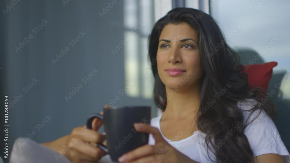 Head and Shoulder shot at a 25 degree angle of a woman sitting on the couch outside in the sun smelling the coffee in her mug and smiling. Continues. Head and Shoulder shot at a 25 degree angle of a woman sitting on the couch outside in the sun smelling the coffee in her mug and smiling. Continues.