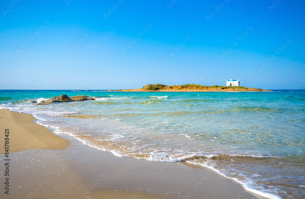 Typical summer image of an amazing pictorial view of a sandy beach with an old white church in a small island at the background, Malia, Crete, Greece.