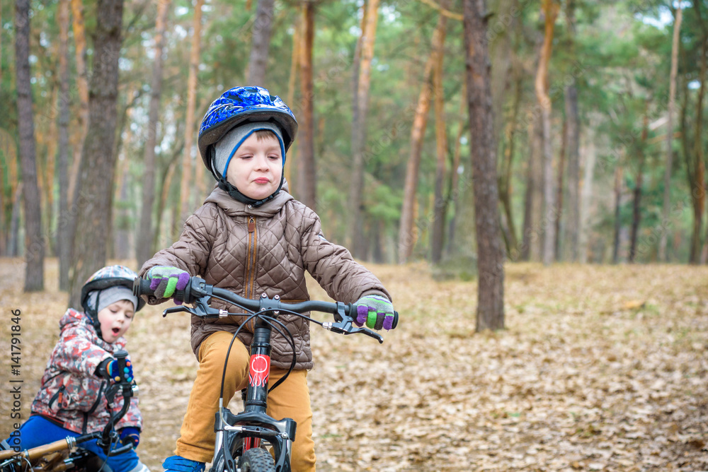 Fototapeta premium Two little siblings having fun on bikes in autumn or spring forest. Selective focus on boy.