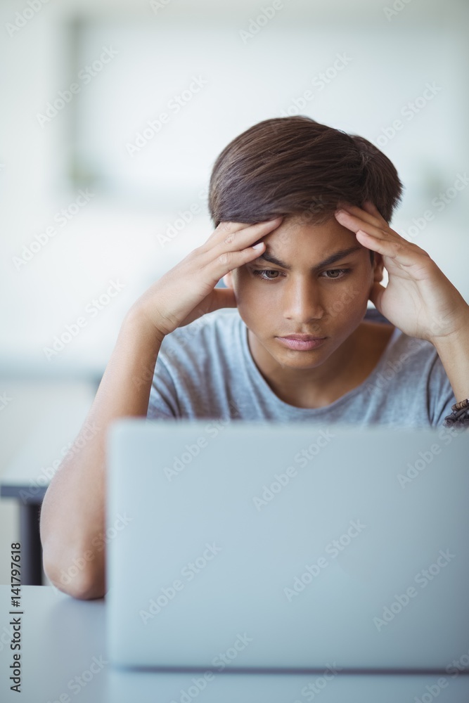 Tensed schoolboy looking at laptop in classroom Tensed schoolboy looking at laptop in classroom