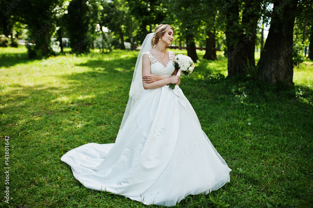Cute blonde bride with wedding bouquet at park on sunny day. Cute blonde bride with wedding bouquet at park on sunny day.