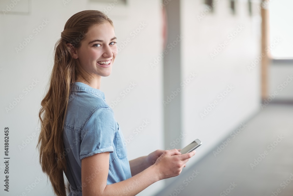 Portrait of happy schoolgirl using mobile phone in corridor Portrait of happy schoolgirl using mobile phone in corridor