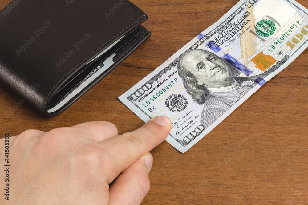 Man has put his finger on the hundred dollar banknote on wooden background, close-up, money and finance concept. Man has put his finger on the hundred dollar banknote on wooden background, close-up, money and finance concept.