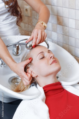 Young blonde woman enjoying hair treatment beauty and people concept happy young woman with hairdresser washing head at hair salon woman resting while she is washing her hair after staining over sink