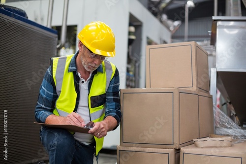 Male factory worker maintaining record on clipboard