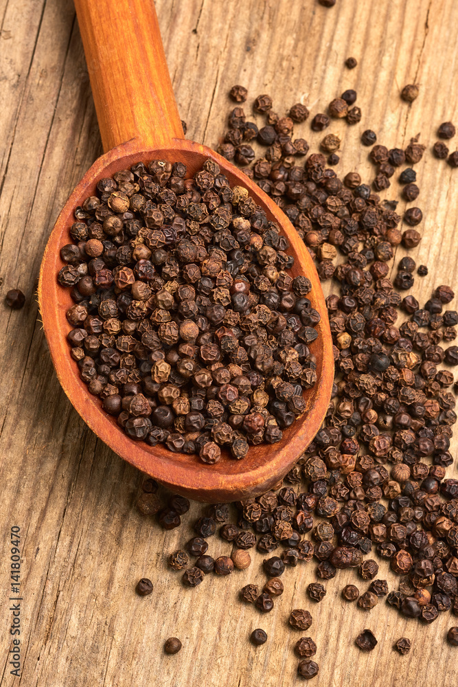 Closeup black pepper whole in wooden spoon on old wooden background Closeup black pepper whole in wooden spoon on old wooden background