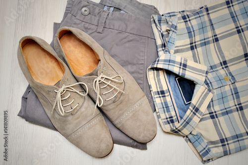 Beige pants, plaid shirt and gray suede shoes. Overhead view of men's casual outfits on white wooden background.