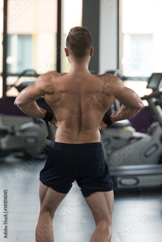 Muscular Man Flexing Back Muscles In Gym