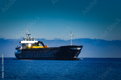 Black cargo ship with long reach excavator moving by baltic sea